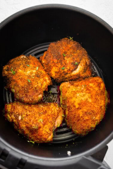 Four bone-in chicken thighs cooked in the basket of an air fryer topped with fresh parsley.