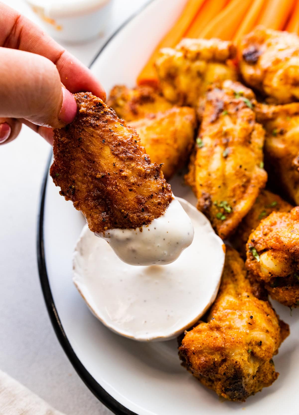 A woman's hand dips an air fried chicken wing into a container of ranch.