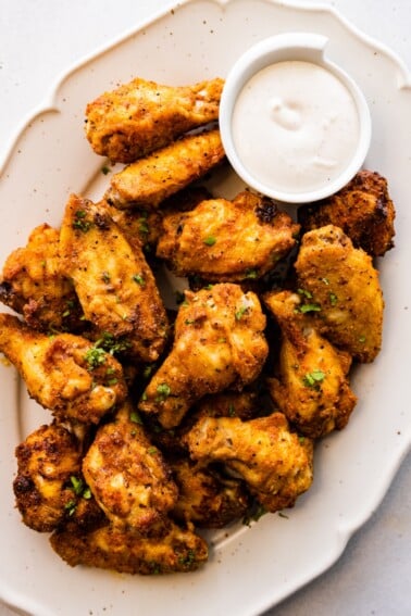 A large plate of air fried chicken wings topped with fresh herbs with a side of ranch.