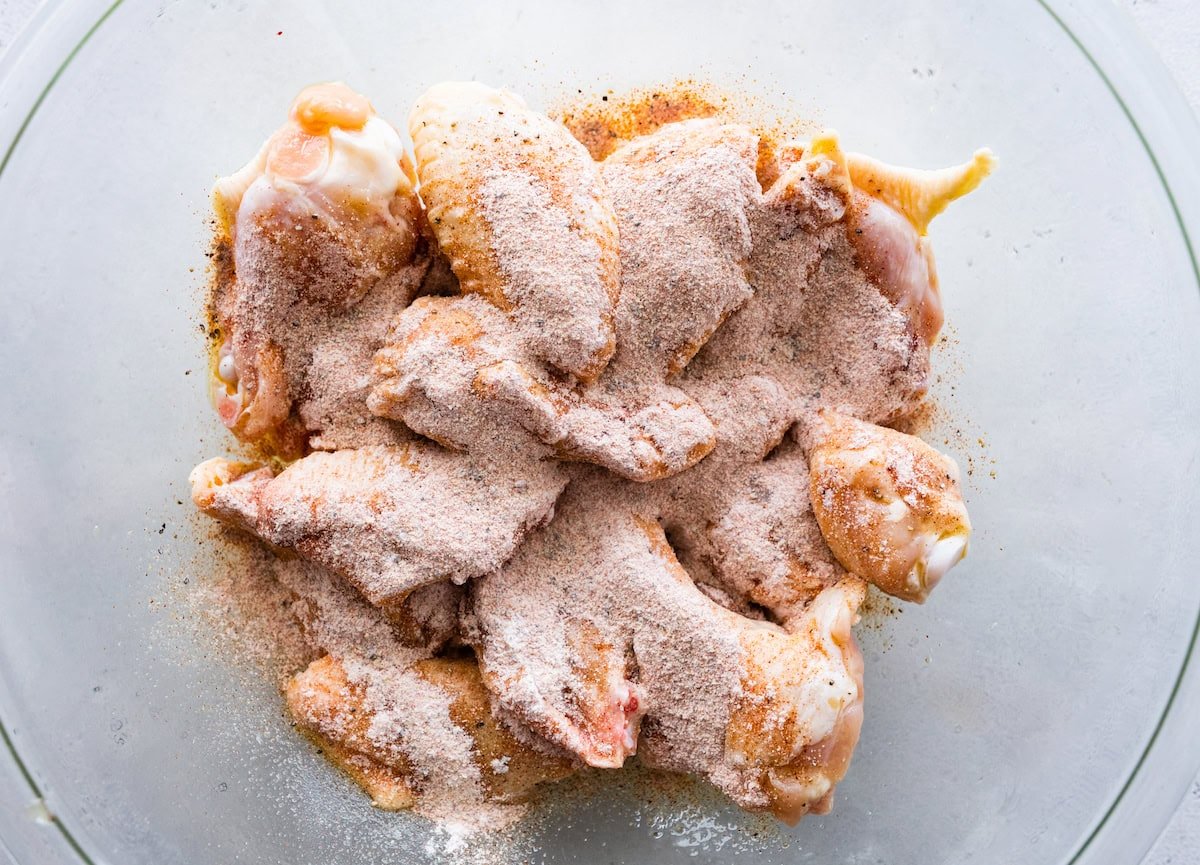 Raw chicken wings in a large bowl coated with seasonings and oil.