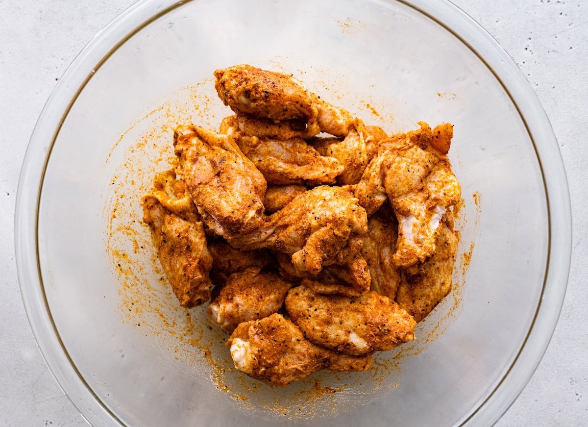 A large bowl of raw chicken wings coated in seasoning and oil.