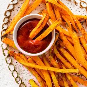 An overhead image of sweet potato fries on a white tray served alongside a small white bowl of ketchup. There are two fries dipped in the ketchup.