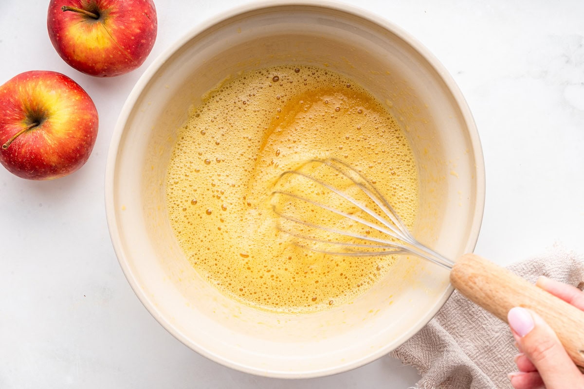 A womans hand uses a whisk to blend together the wet ingredients for an applesauce cake.