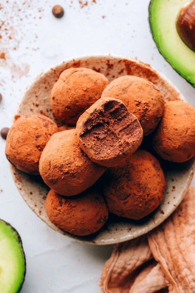 4-Ingredient Chocolate Avocado Truffles // Rich, creamy and so delicious. #vegan #glutenfree An overhead photo of a bowl of avocado truffles. The top truffle has a bite taken out of it.