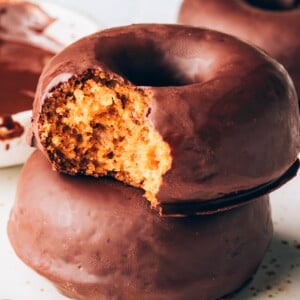 A stack of two donuts. The top donut has a bite taken out of it.