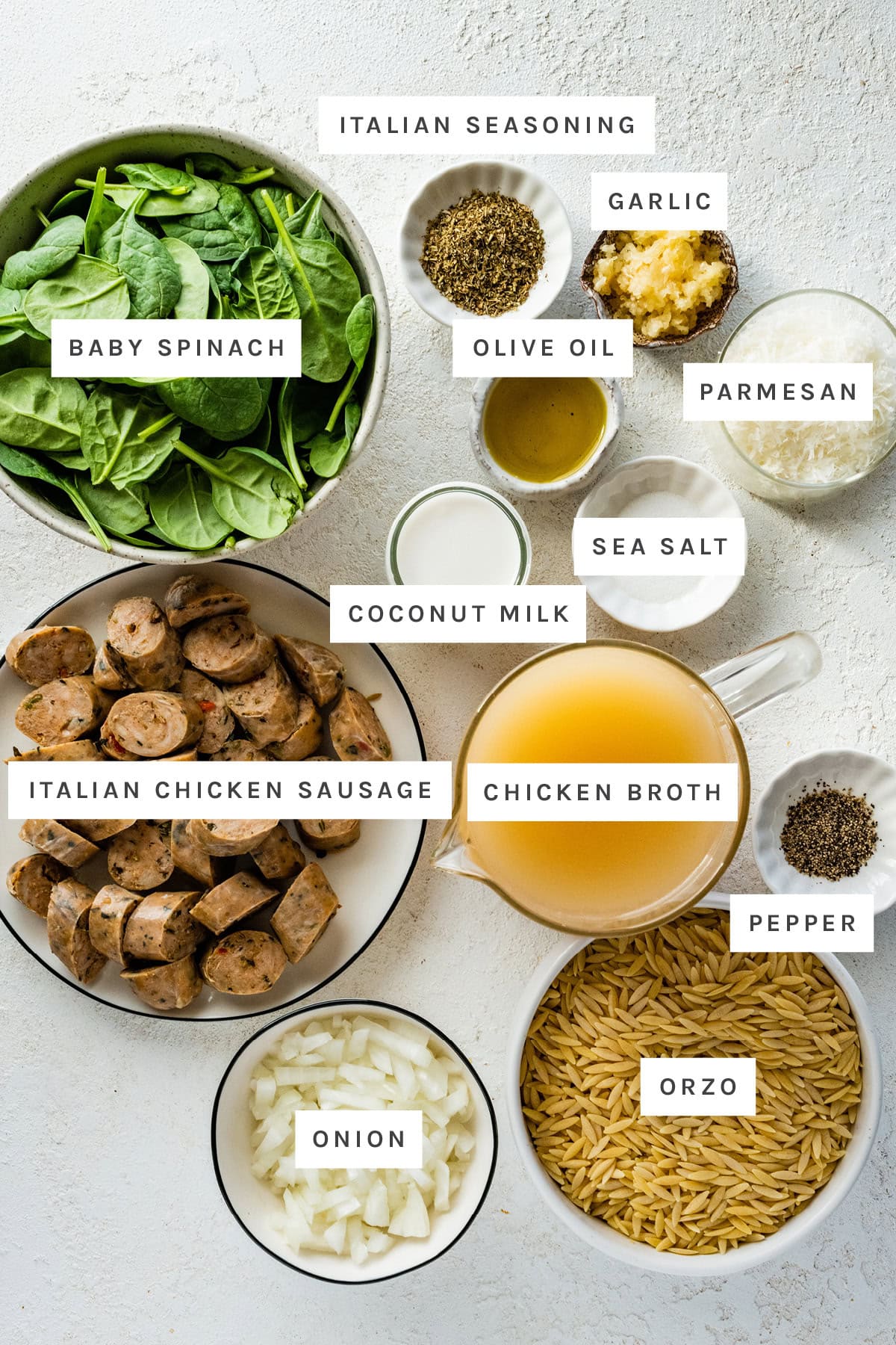 Ingredients measured out to make One Pan Chicken Sausage and Orzo: baby spinach, Italian seasoning, garlic, olive oil, parmesan, sea salt, coconut milk, chicken broth, Italian chicken sausage, pepper, onion and orzo.