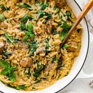 A white Dutch oven with creamy orzo, chicken sausage and spinach mixed together.