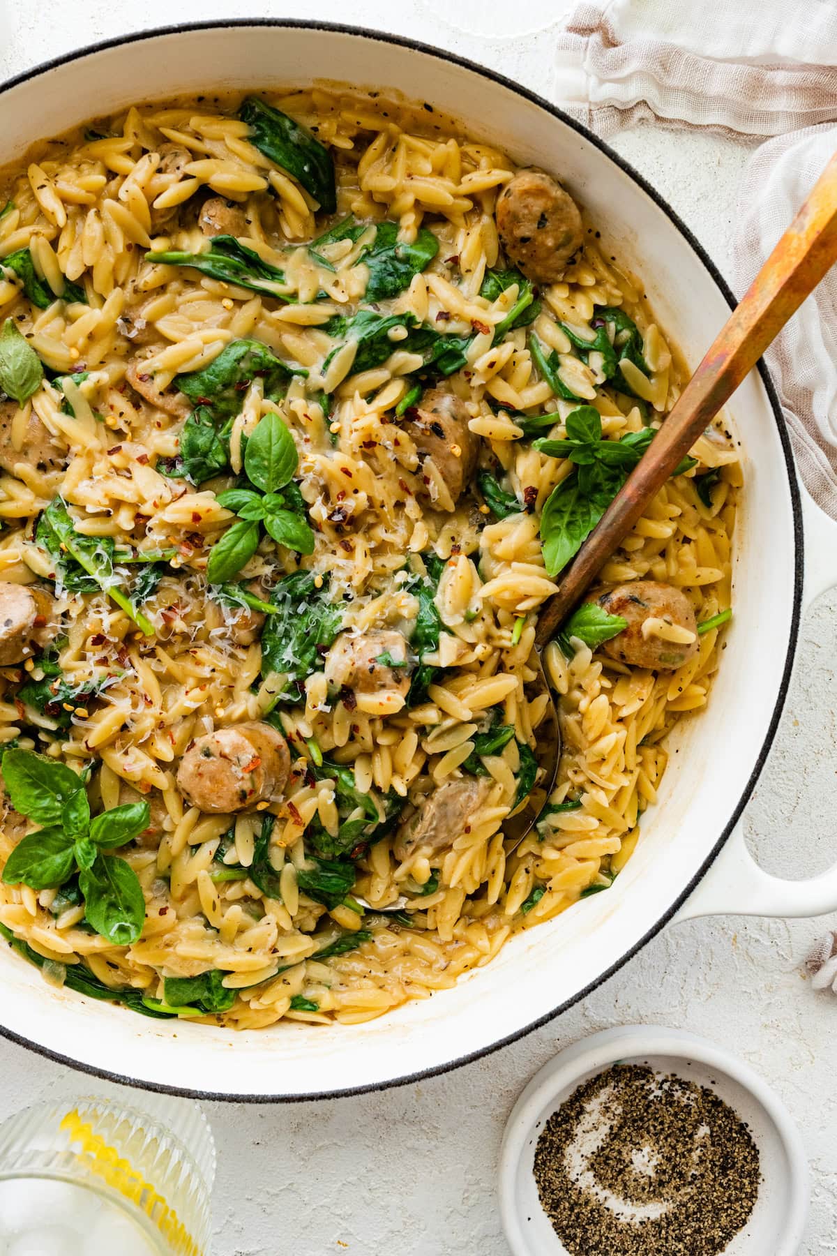 A white Dutch oven with creamy orzo, chicken sausage and spinach mixed together.