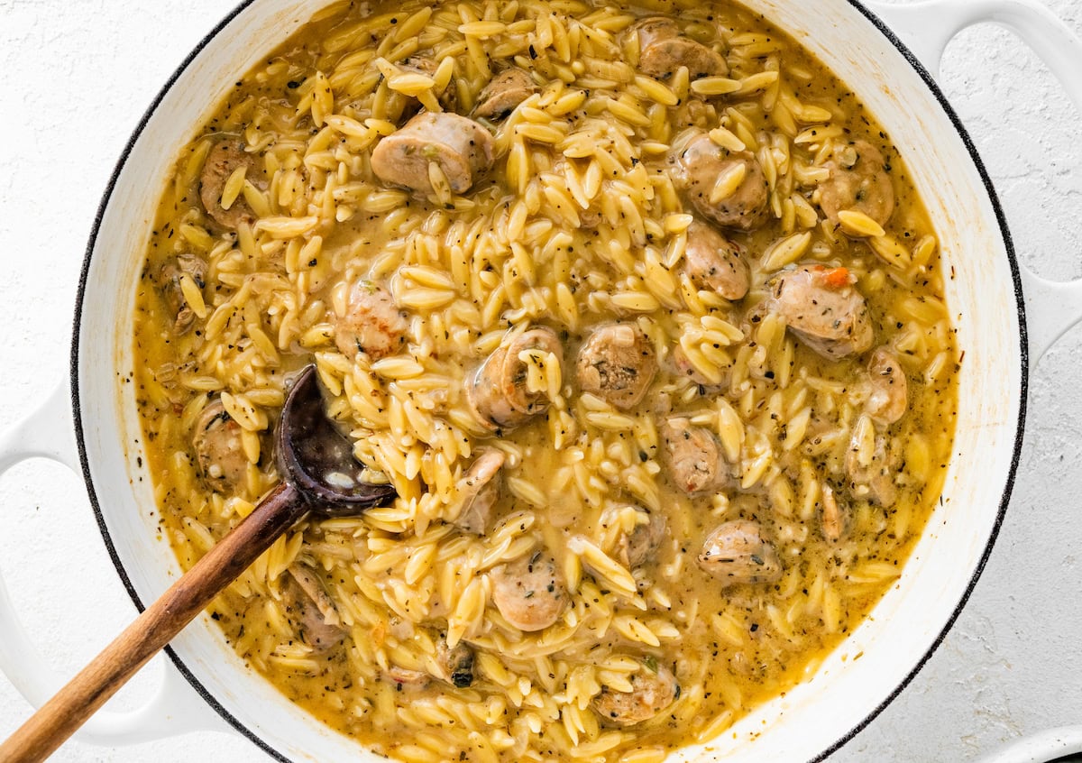 A white Dutch oven cooked orzo and chicken sausage.