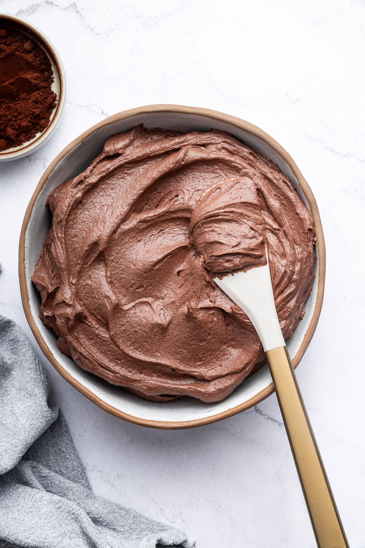 Chocolate buttercream frosting in a bowl with a white spatula.