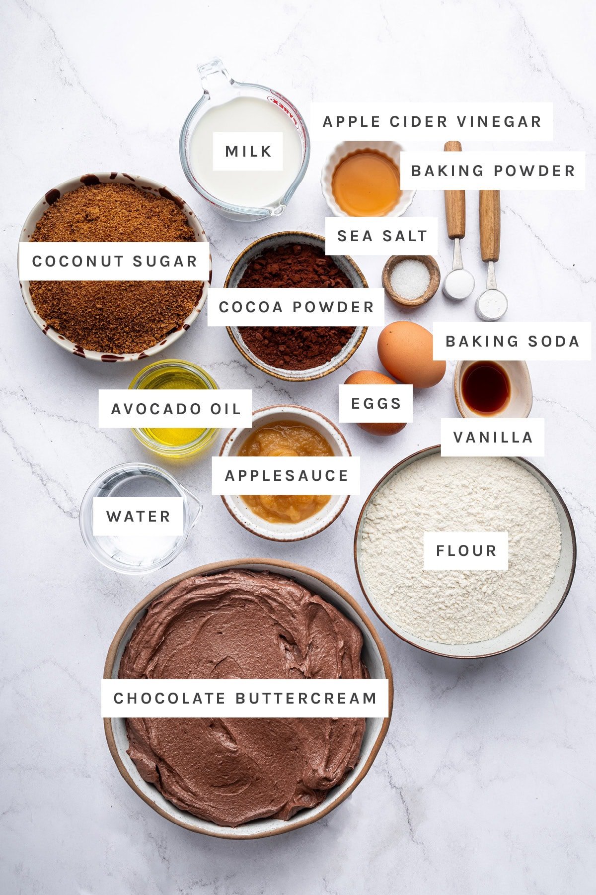 Ingredients measured out to make Healthy Chocolate Cake: coconut sugar, milk, apple cider vinegar, baking powder, sea salt, cocoa powder, baking soda, eggs, avocado oil, applesauce, vanilla, water, flour and chocolate buttercream.