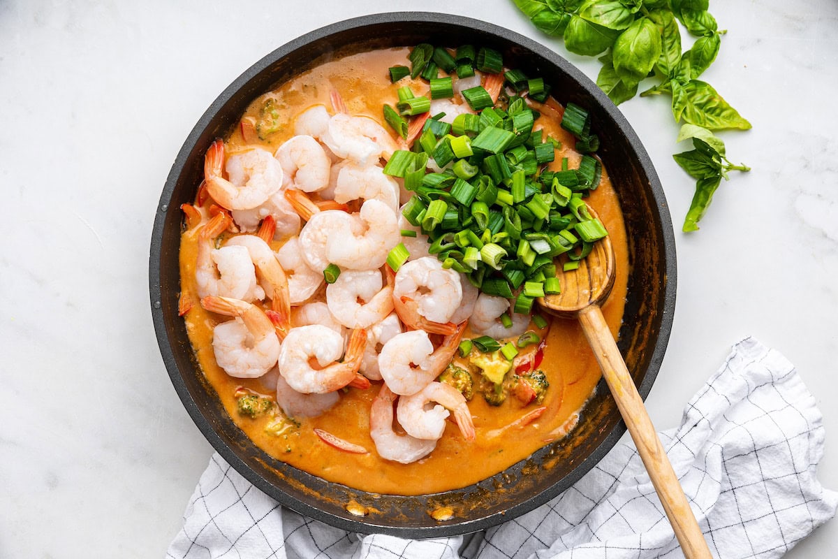 A skillet with a raw shrimp and scallions added to the vegetable curry mix.