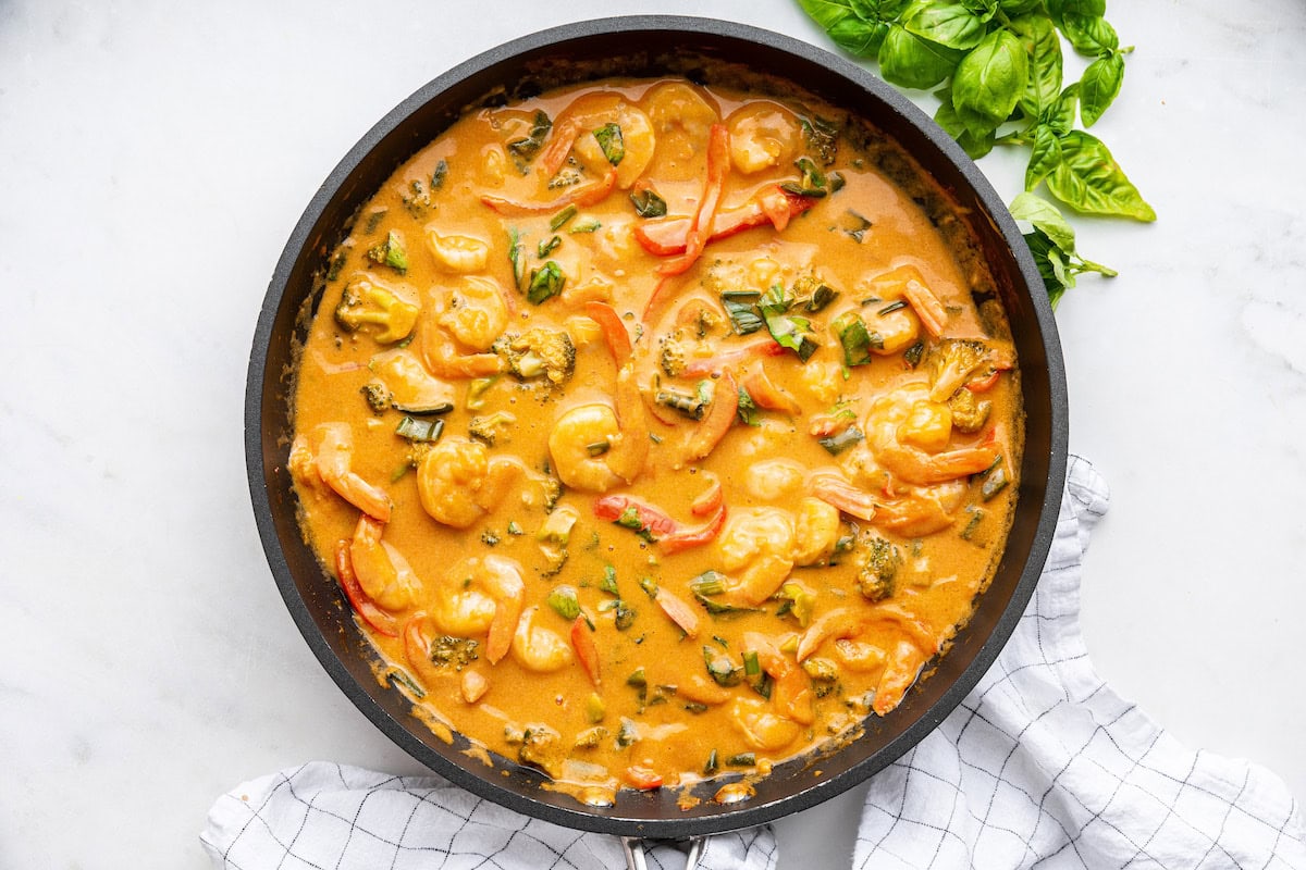 A skillet of coconut shrimp curry with some fresh basil leaves to the side.