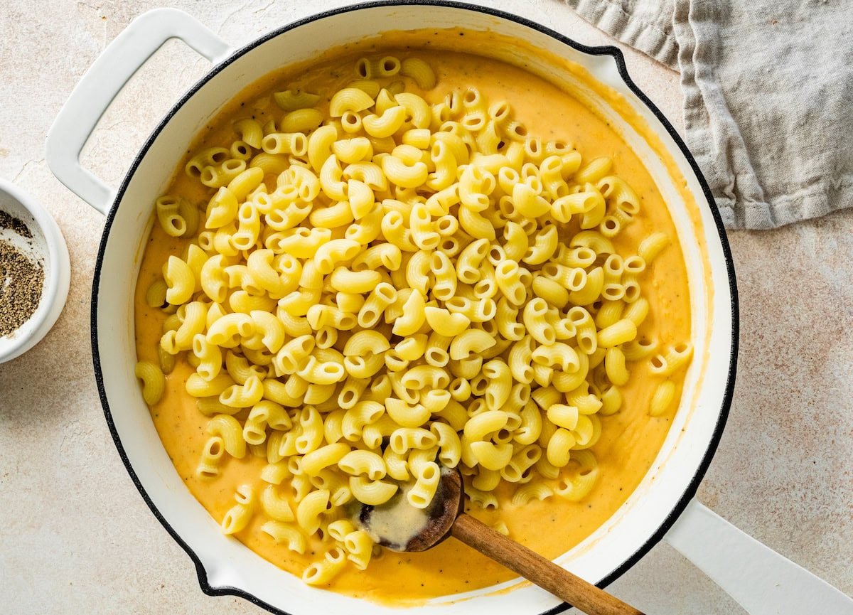 Macaroni noodles added to a large pot of cottage cheese sauce.