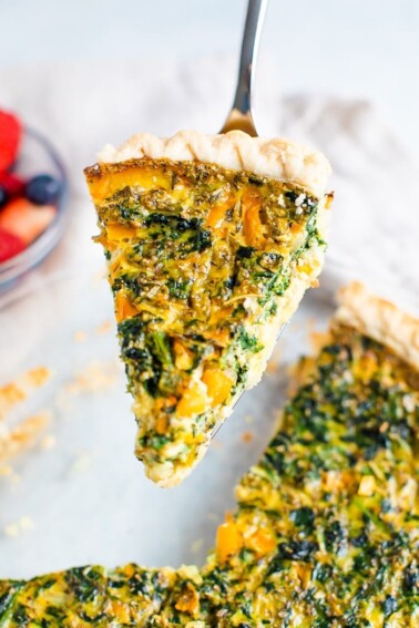 Spatula lifting a slice of spinach quiche from the pie.