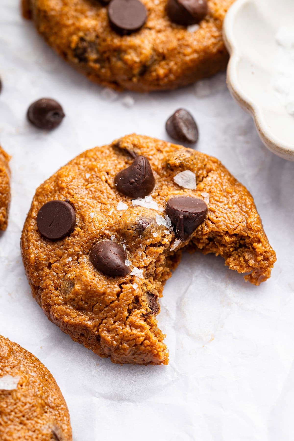One flourless peanut butter cookie with chocolate chips with a bite taken out of it.