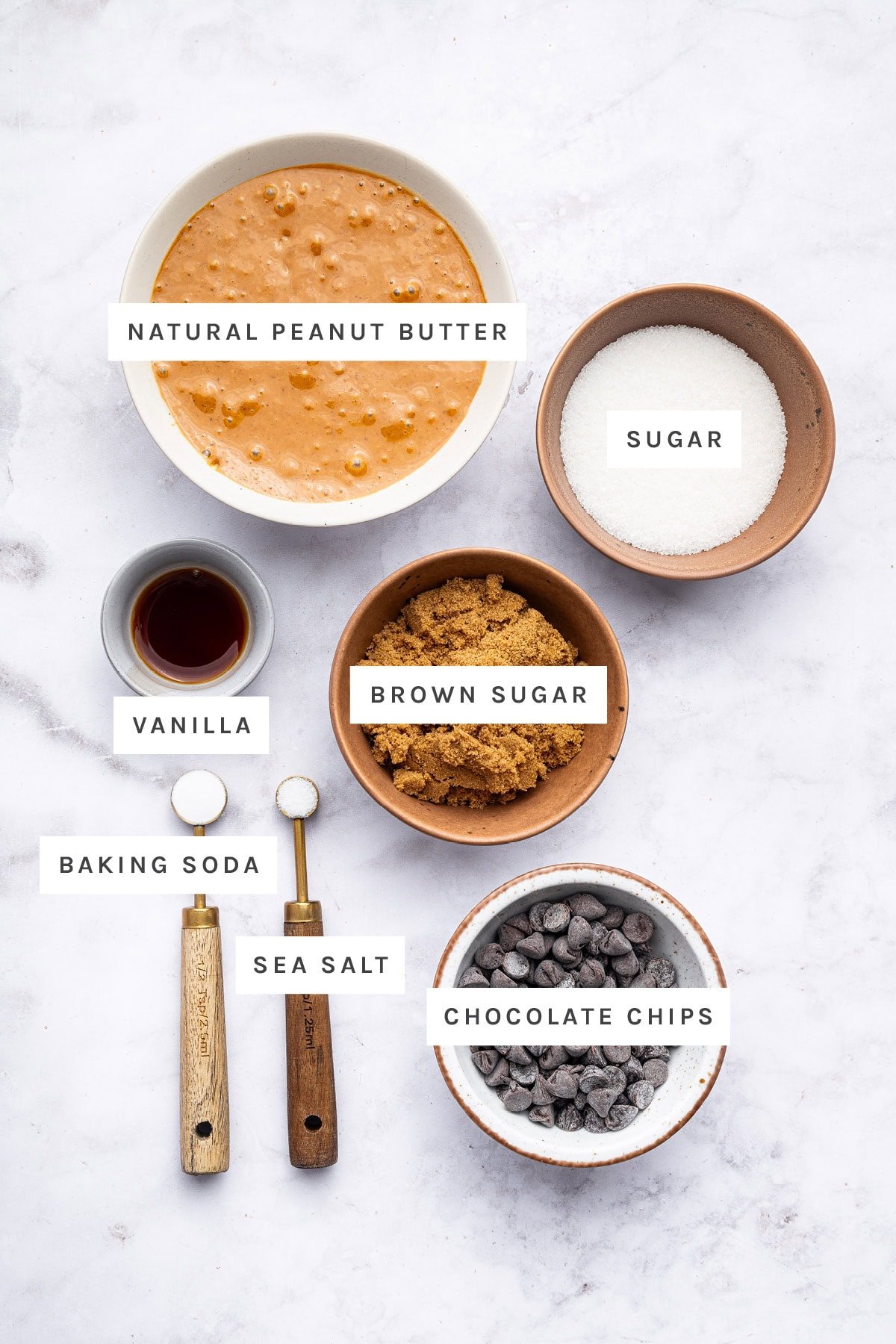 Ingredients measured out to make Flourless Peanut Butter Cookies: natural peanut butter, sugar, vanilla, brown sugar, baking soda, sea salt and chocolate chips.