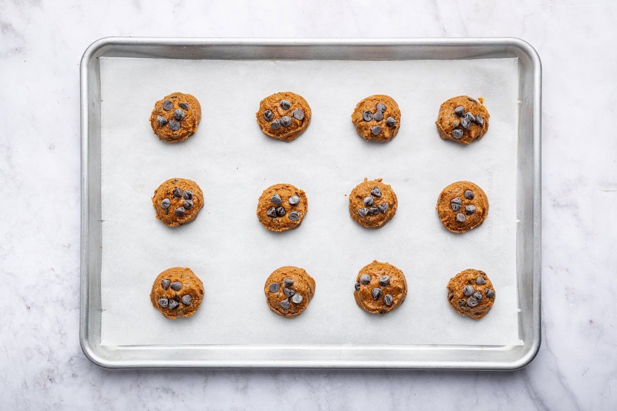 12 unbaked flourless peanut butter cookies with chocolate chips on a baking sheet lined with parchment paper.