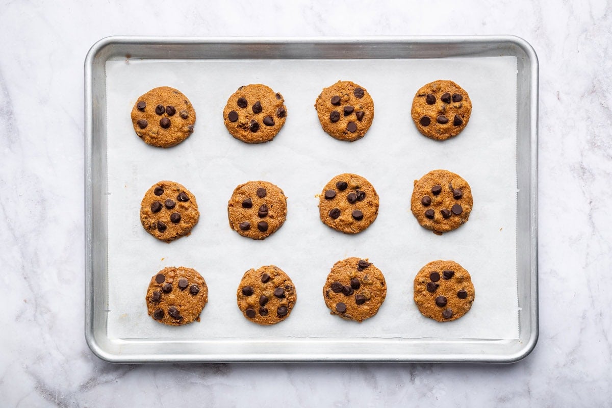 12 baked flourless peanut butter cookies with chocolate chips on a baking sheet lined with parchment paper.
