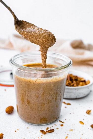 A spoonful of granola butter dripping into a glass weck jar.