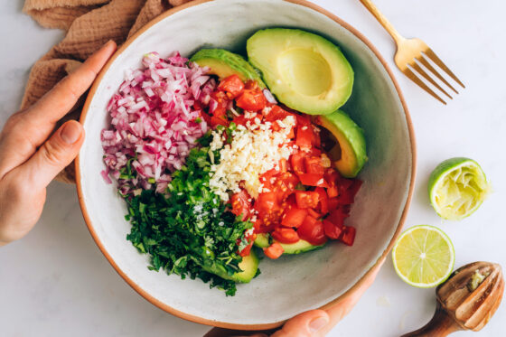 Avocado halves, tomato, red onion, cilantro, garlic and lime juice in a bowl.