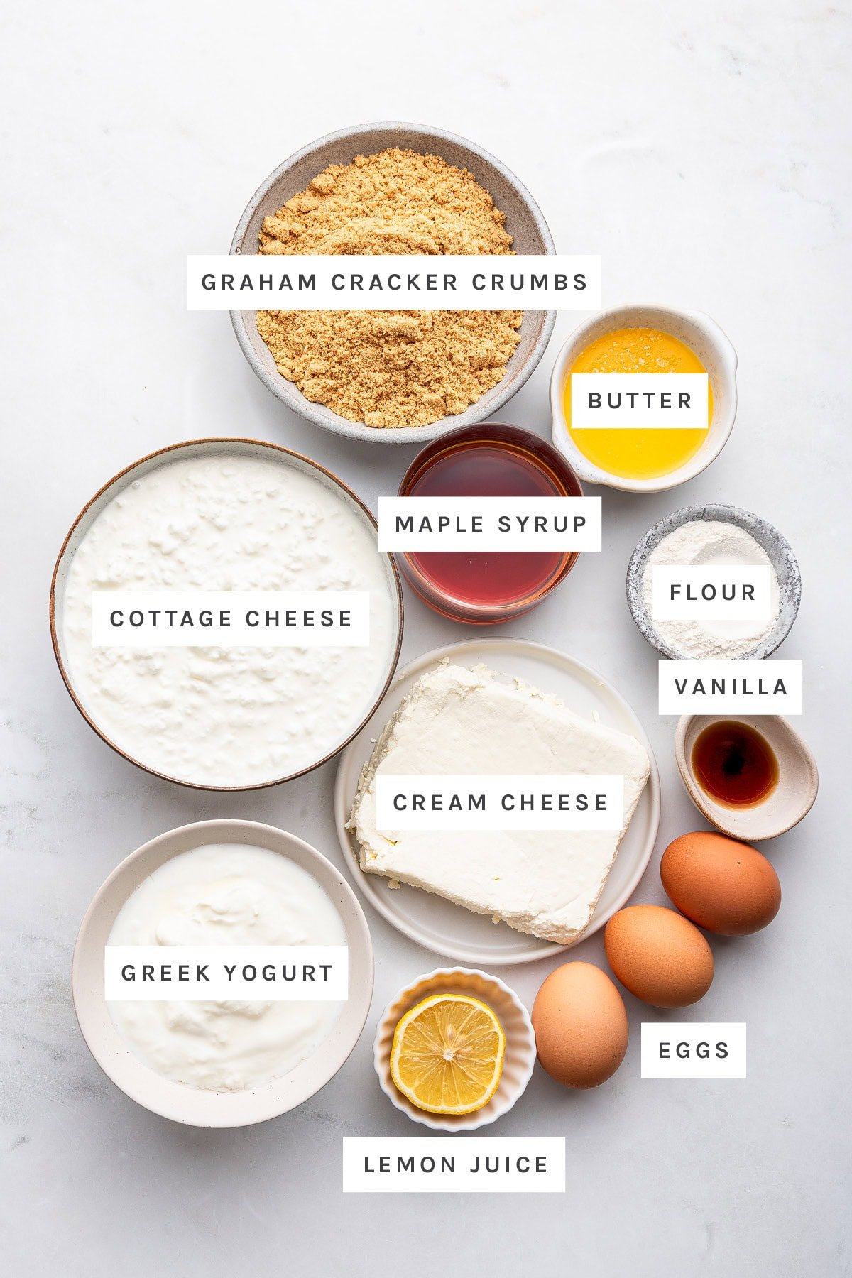 Ingredients measured out to make Healthy Cheesecake: graham cracker crumbs, butter, maple syrup, flour, vanilla, cottage cheese, cream cheese, eggs, Greek yogurt and lemon juice.