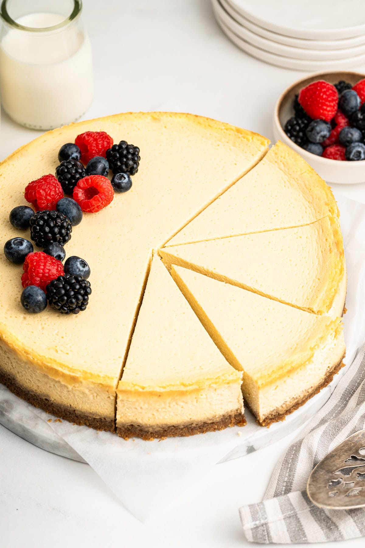 The full healthy cheesecake served with fresh berries on top. Four slices have been cut from the cheesecake.