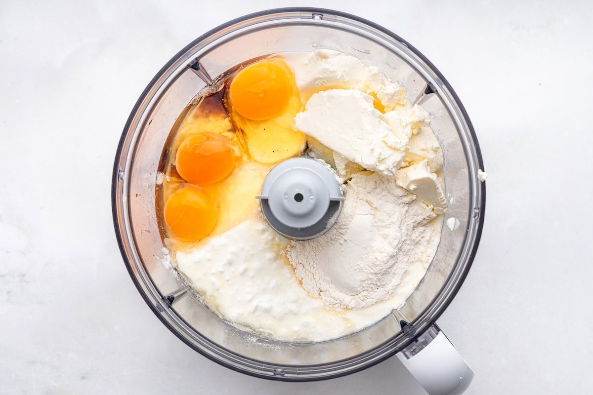 Cottage cheese, greek yogurt, cream cheese, eggs, maple syrup, vanilla extract, flour and lemon juice in the bowl of a food processor.