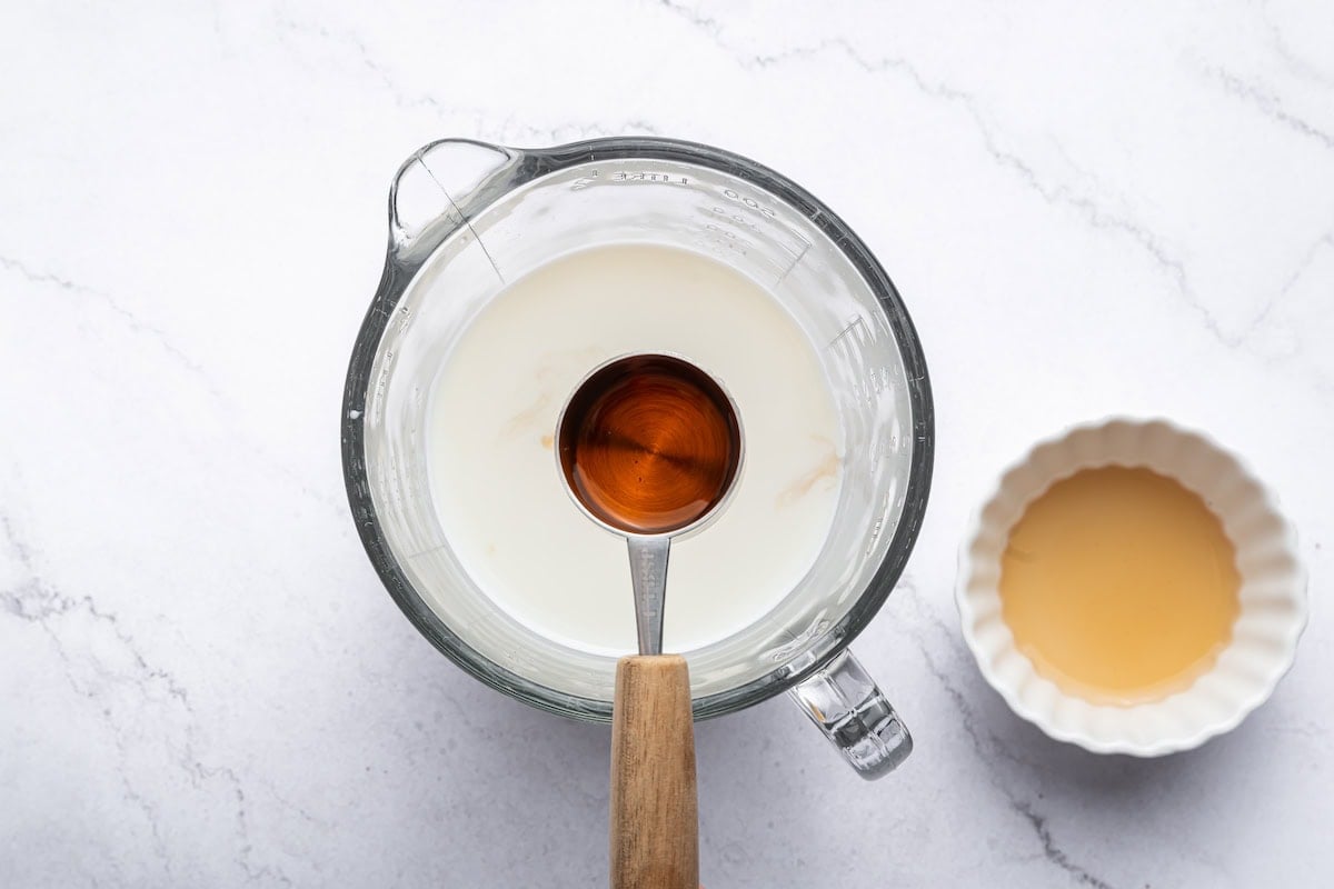 A teaspoon of vanilla extract held over a cup of milk.