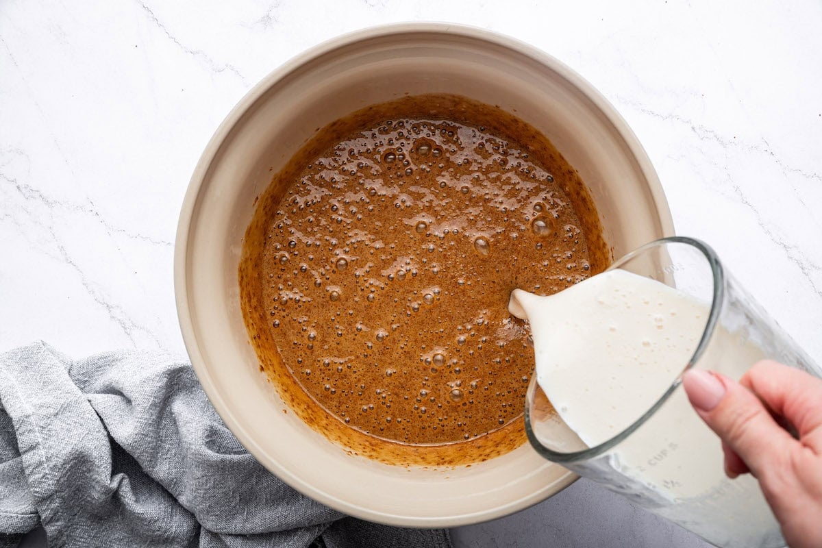 Milk is being poured into a large mixing bowl of a chocolate batter used to make a cake.