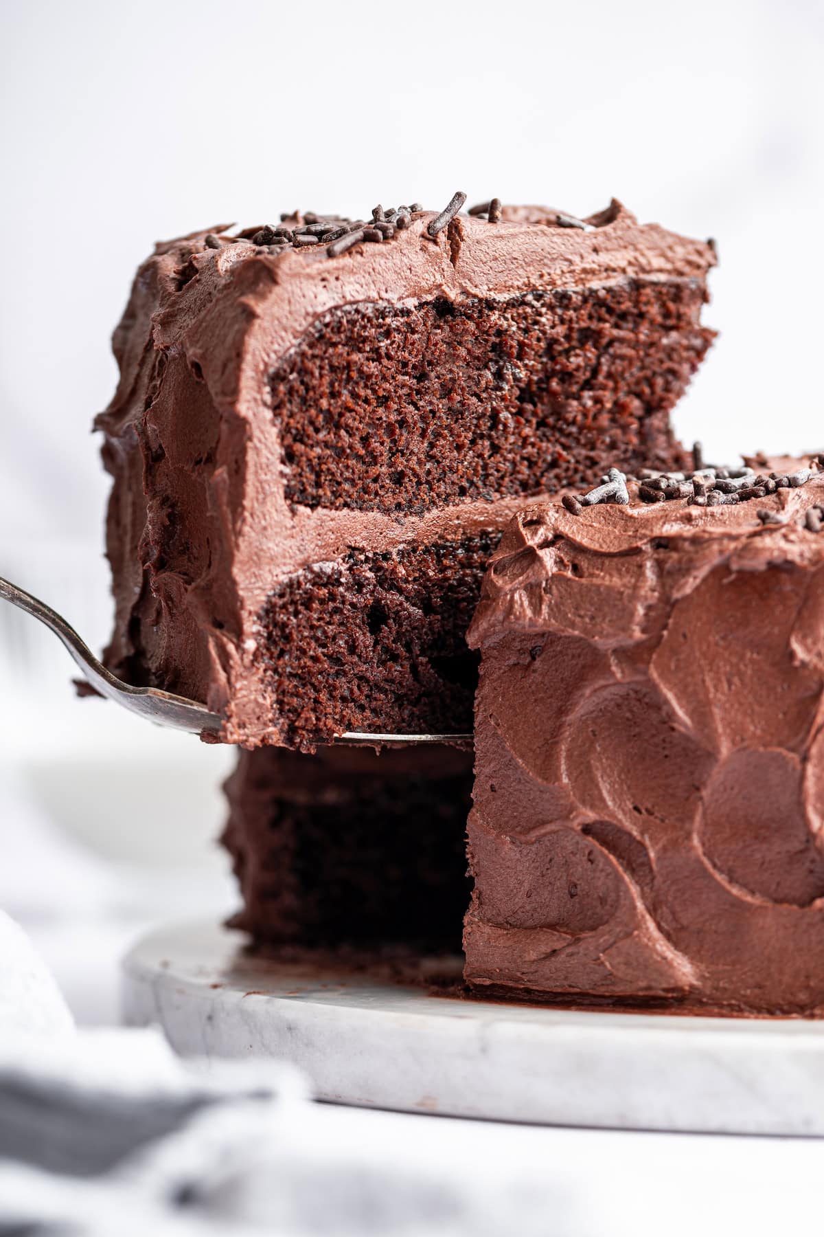 A slice of chocolate cake is lifted away from the whole cake by a metal spatula.