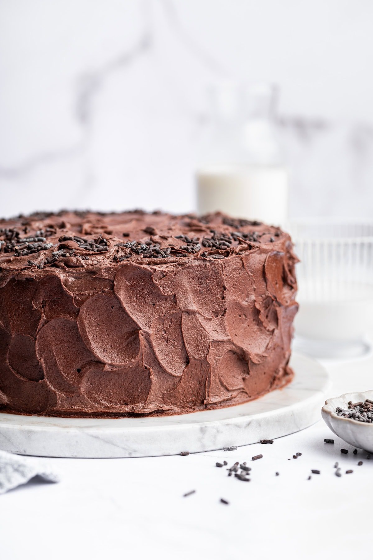 A chocolate cake with chocolate buttercream frosting and chocolate sprinkles on top.