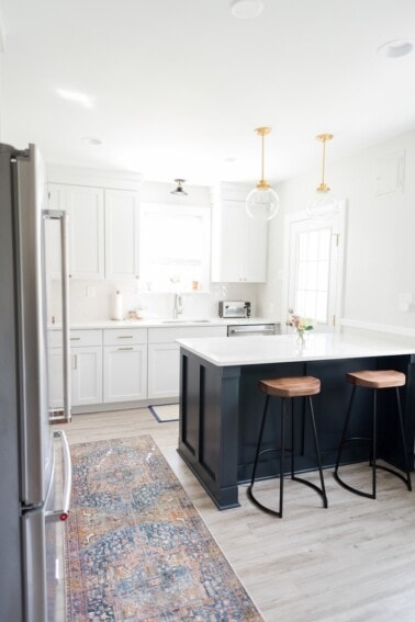 White kitchen with navy blue island and wood and metal modern stools.