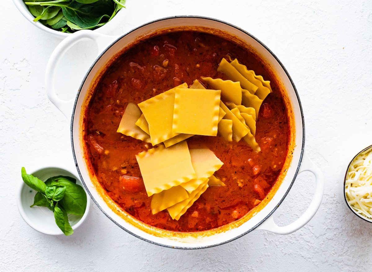 Lasagna noodles in a large pot with marinara sauce, herbs, spices, sausage, and vegetables.