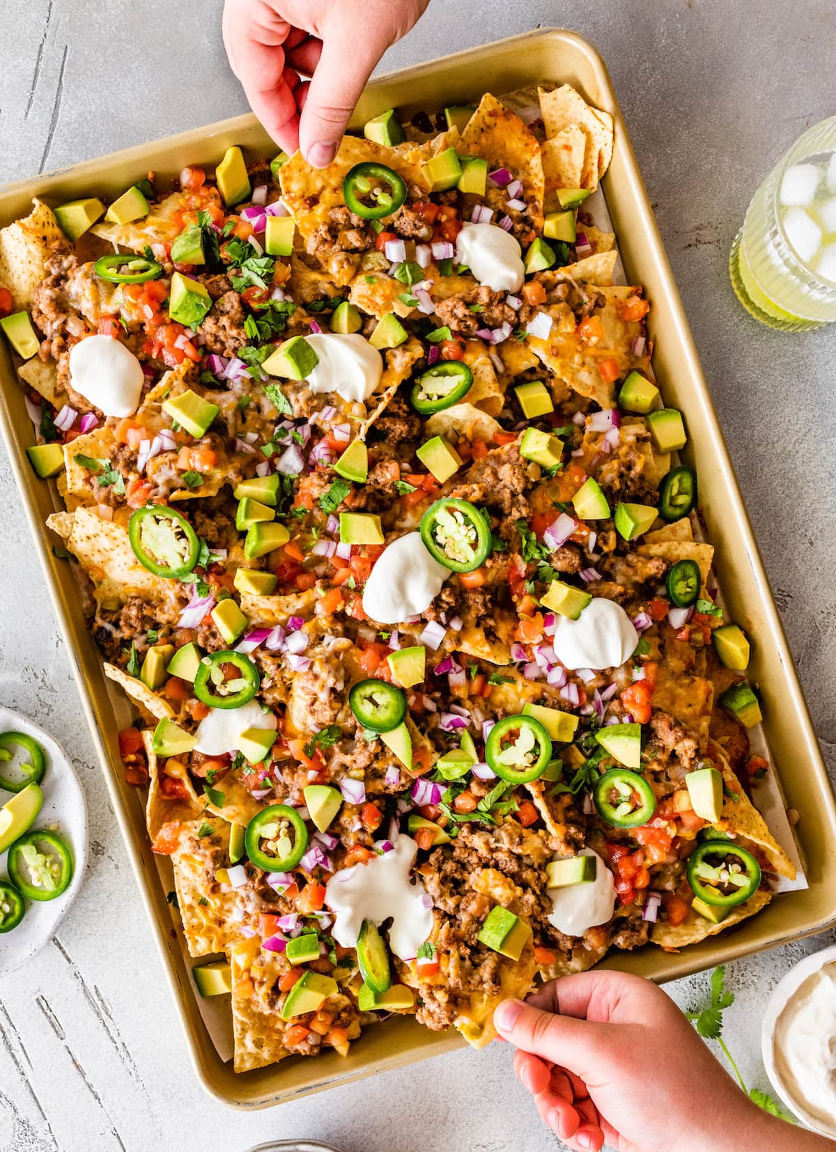 Loaded nachos on a baking tray with meat, jalapeños, sour cream, avocado, cheese, and more.