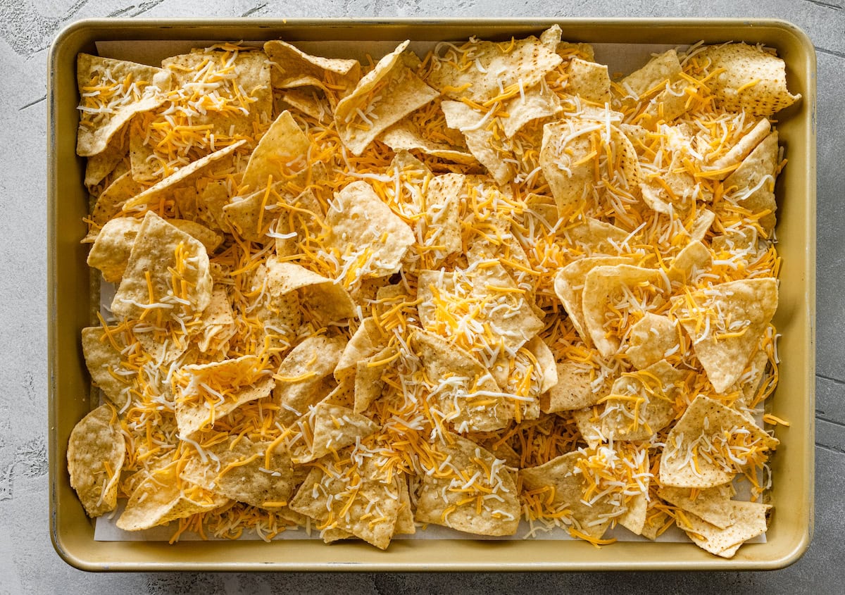 Shredded cheese spread over tortilla chips on a baking tray.