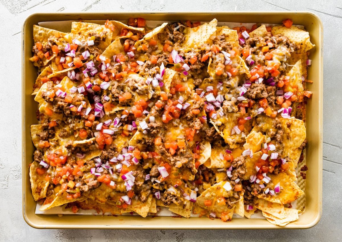 Loaded nachos on a baking tray with cheese, onion, tomato, meat, and beans.