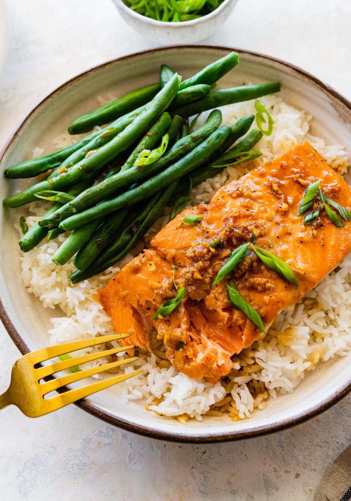 A fork is about to take a piece of maple glazed salmon the is on a bed of rice with a side of green beans.
