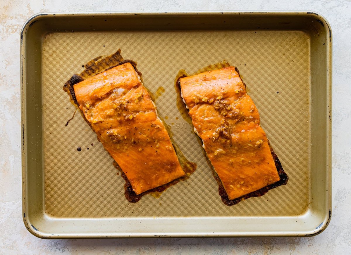 Two marinated salmon filets on a baking tray after being baked.
