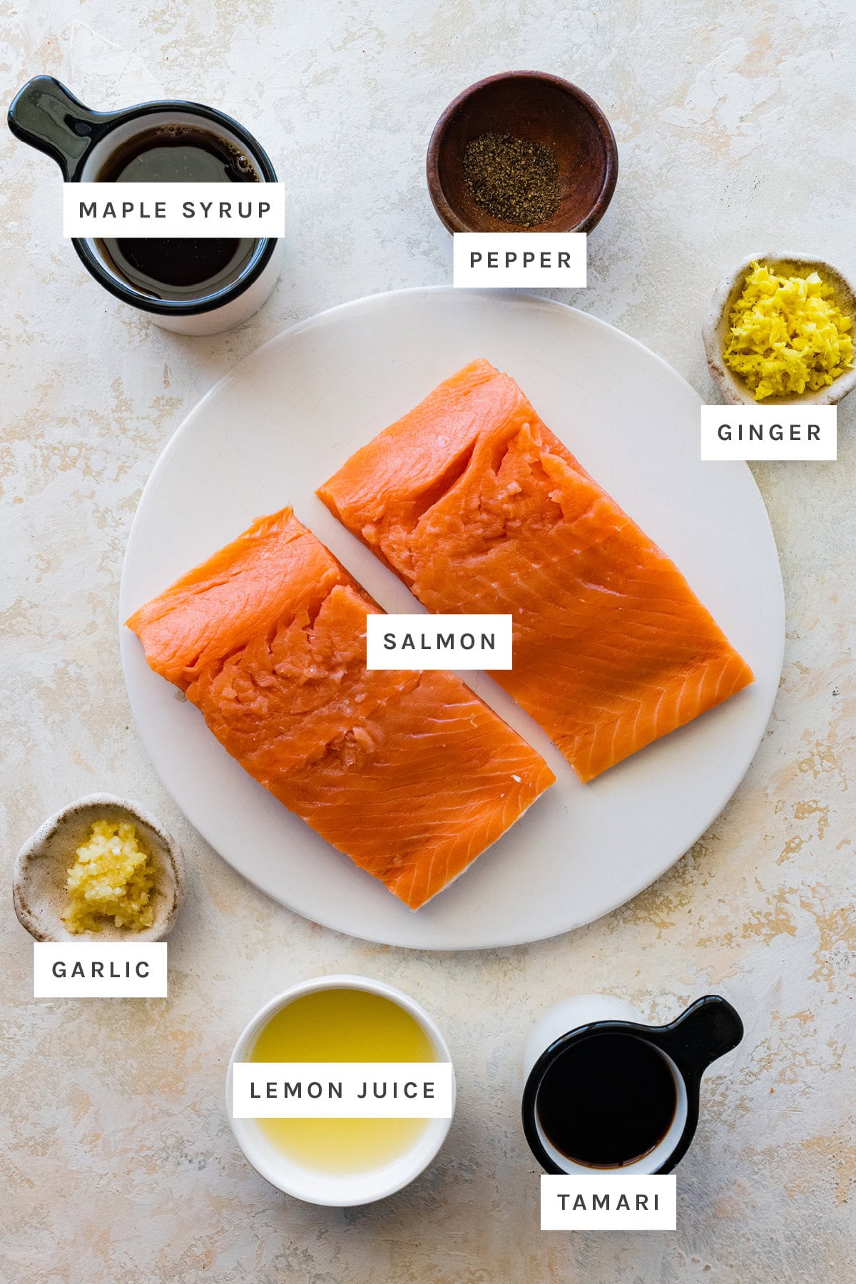 Ingredients measured out to make Maple Glazed Salmon: maple syrup, pepper, ginger, salmon, garlic, lemon juice and tamari.
