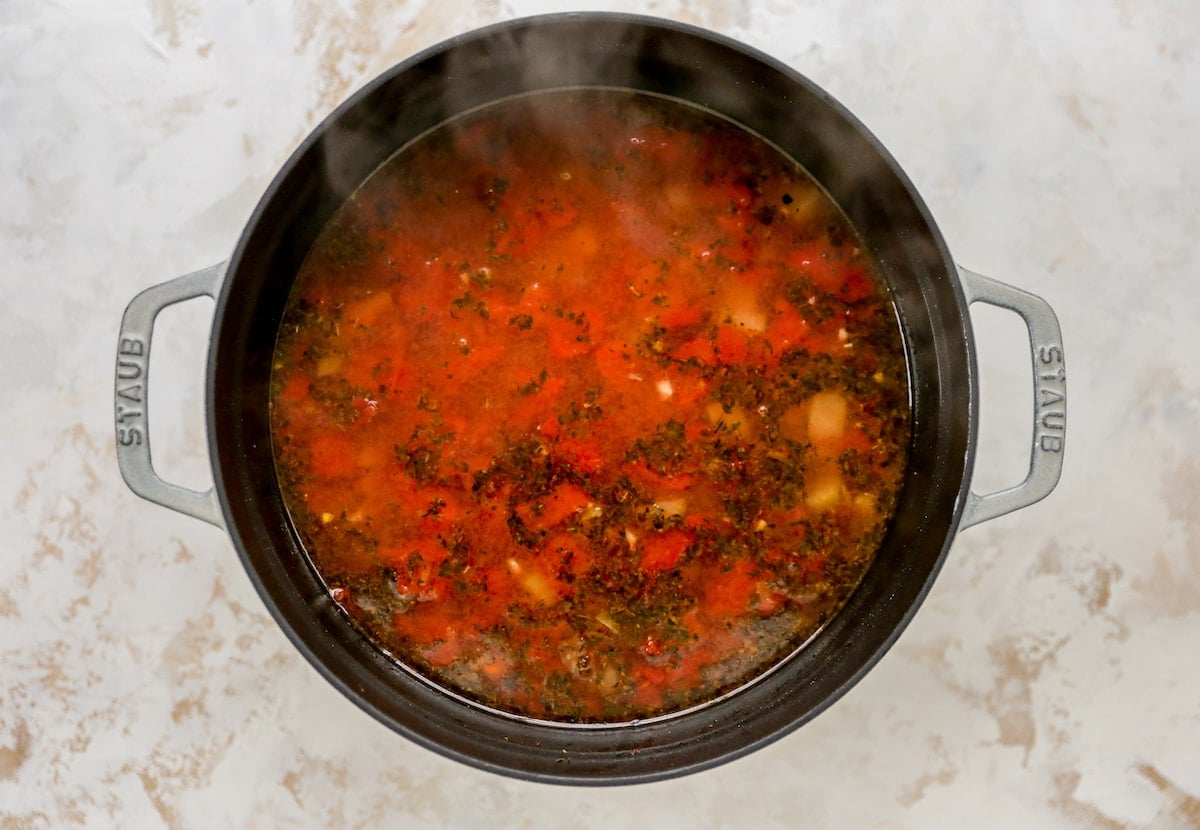 A large pot with veggies for minestrone soup, vegetable broth has just been added to the pot.