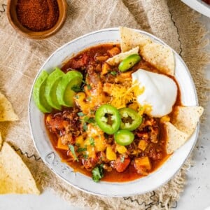 A bowl of no bean chili topped with cheese, jalapeños, avocado, sour cream and chips.