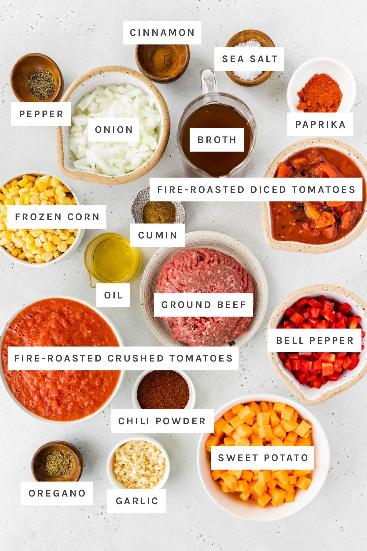 Ingredients measured out to make no-bean chili: pepper, cinnamon, sea salt, paprika, onion, broth, fire-roasted tomatoes, cumin, frozen corn, oil, ground beef, bell pepper, fire-roasted crushed tomatoes, chili powder, sweet potato, garlic and oregano.