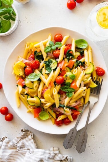 A serving of pasta primavera on a plate topped with fresh herbs.