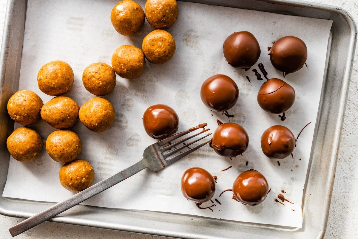 Peanut butter balls on a tray with half of them being covered in chocolate.