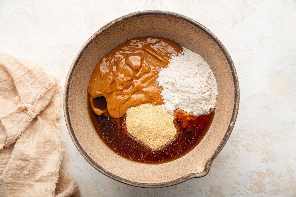 Peanut butter, oat flour, graham cracker crumbs and maple syrup in a mixing bowl.