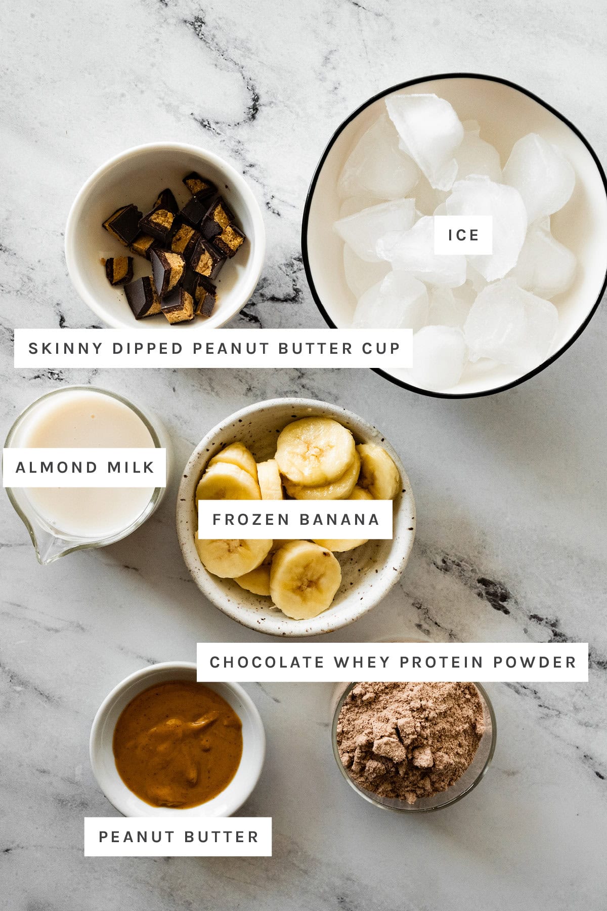 Ingredients measured out to make Peanut Butter Cup Protein Fluff: Skinny Dipped peanut butter cup, ice, almond milk, frozen banana, chocolate whey protein powder and peanut butter.