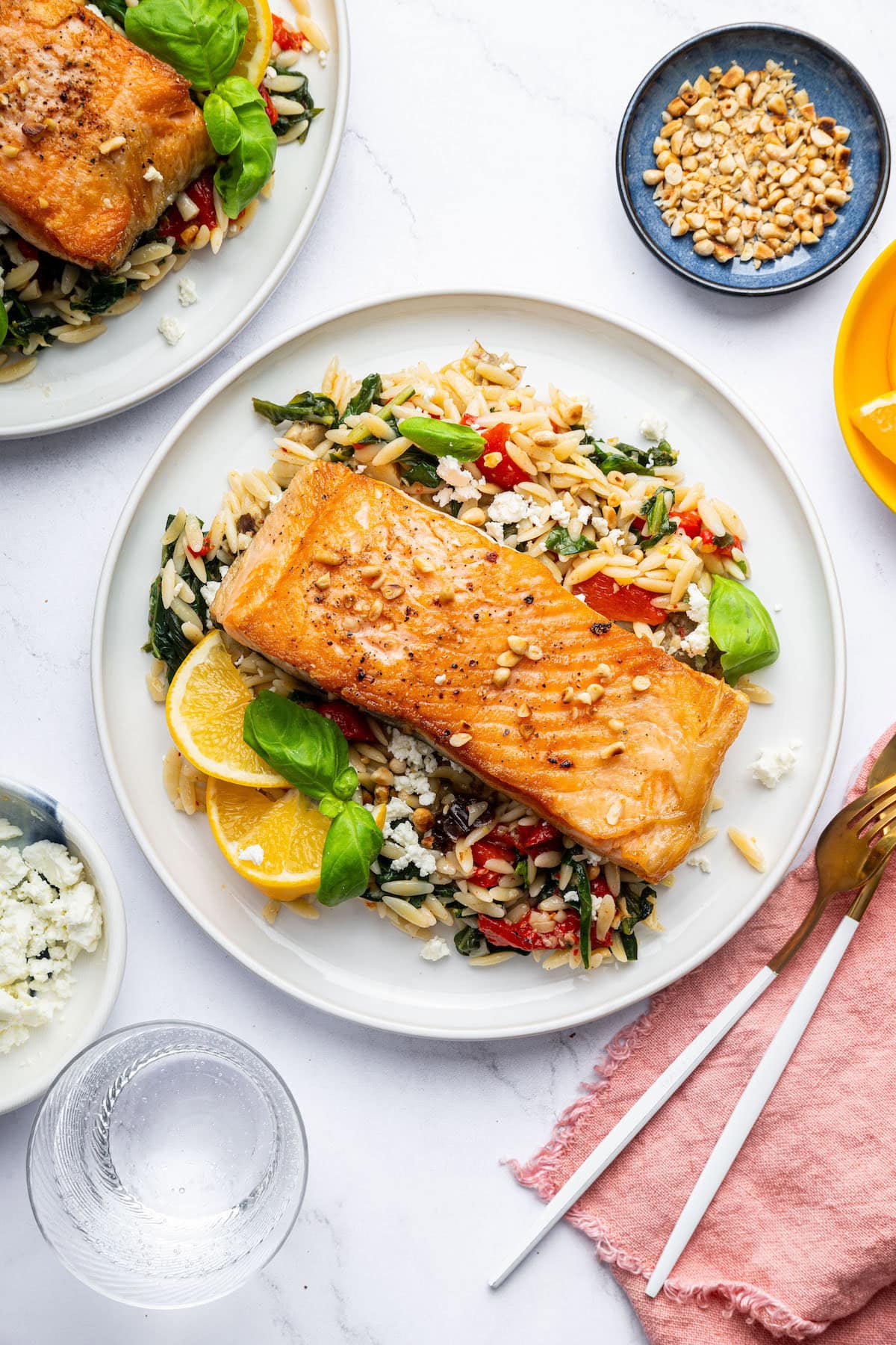 A salmon filet served on a white plate over a bed of orzo combined with roasted red peppers, chopped dates, feta and swiss chard.