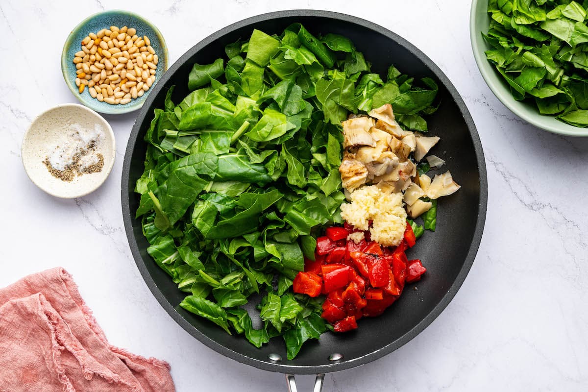 A skillet with swiss chard, roasted red peppers, artichoke hearts and garlic.
