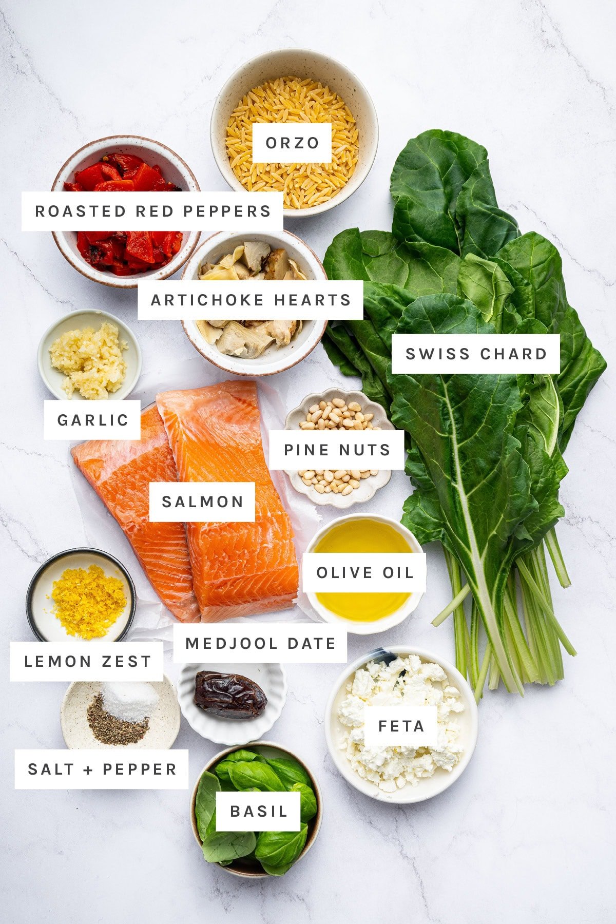 Ingredients measured out to make Mediterranean Salmon and Orzo Skillet: roasted red peppers, orzo, artichoke hearts, swiss chard, garlic, pine nuts, salmon, olive oil, lemon zest, medjool date, salt, pepper, basil and feta.